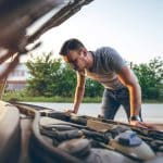 Jeune homme qui regarde sous le capot de sa voiture pour la réparer