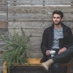 jeune homme assis sur un banc à côé d'une plante tenant une tasse